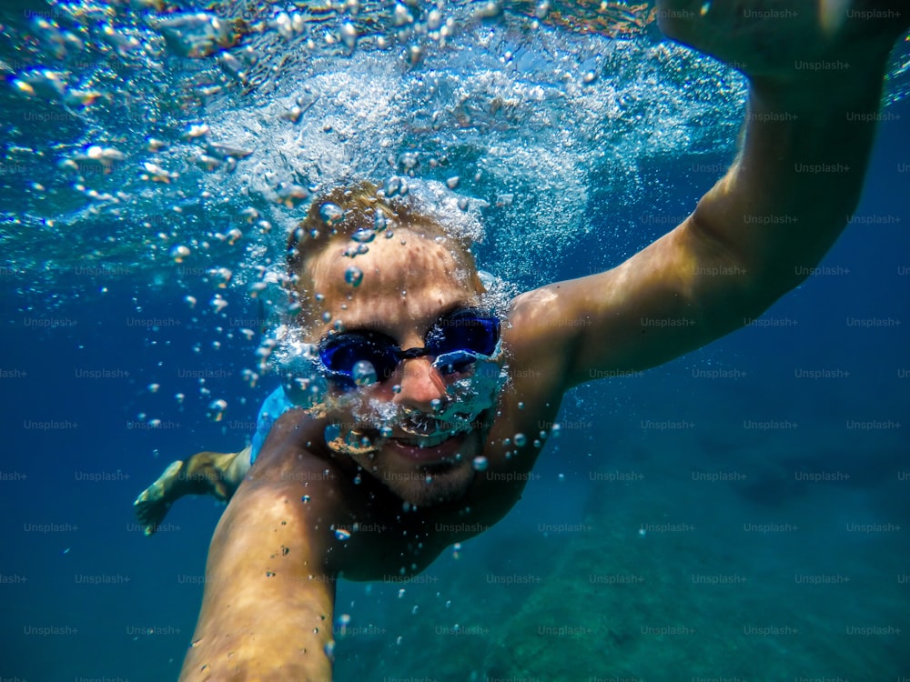 Vue sous-marine d’un jeune plongeur nageant et profitant de la mer pour les vacances d’été tout en prenant un selfie.