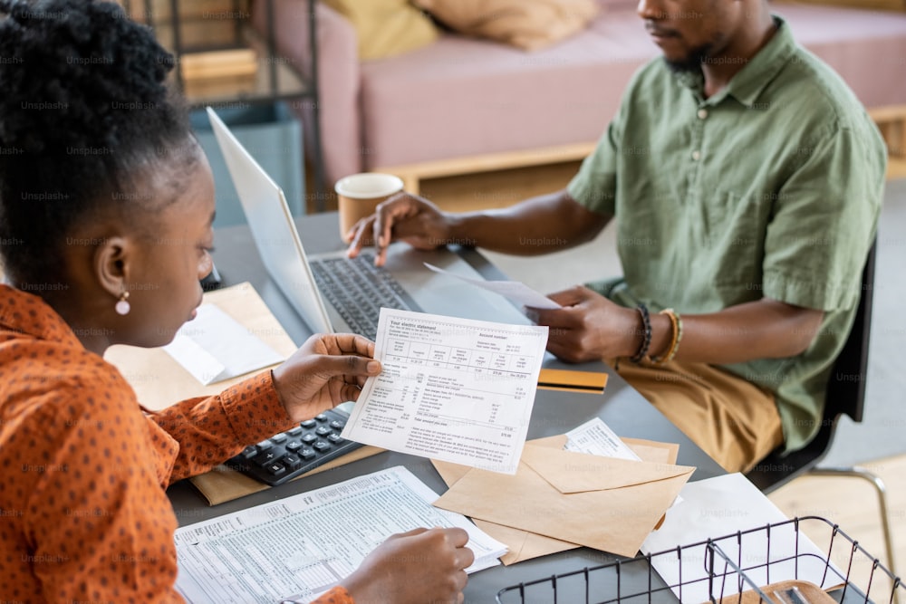 Nahaufnahme eines afroamerikanischen Paares, das mit Papieren am Tisch sitzt und zu Hause das Budget untersucht