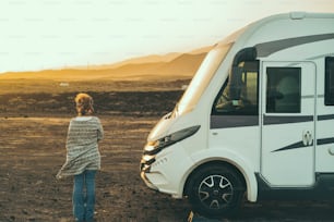 Alternative tourist vanlife concept with standing woman in back view near a big camper van motornohome enjoying the freedom and desert scenic nature place. Travel people lifestyle