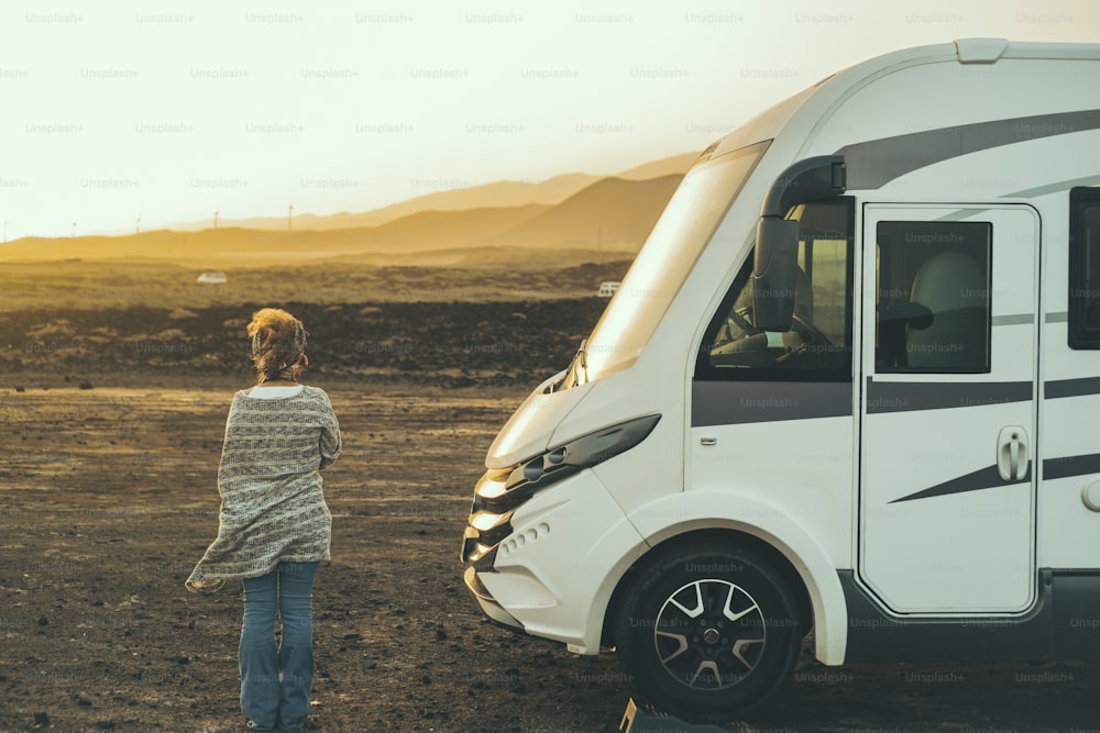 Alternative tourist vanlife concept with standing woman in back view near a big camper van motornohome enjoying the freedom and desert scenic nature place. Travel people lifestyle