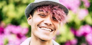 Happy cheerful handsome trendy alternative young man teenager portrait smiling on camera with coloured flower park background - diversity and youthful people with joy