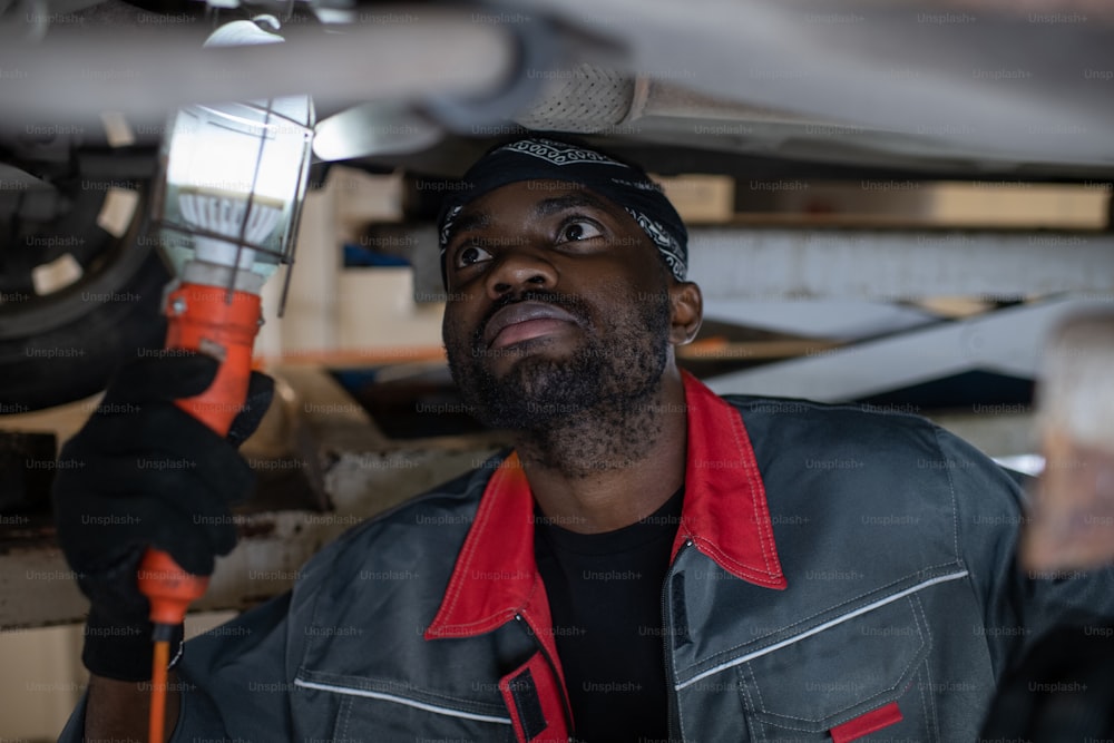 Portrait of African-American mechanic inspecting car on vehicle lift in auto repair shop, copy space