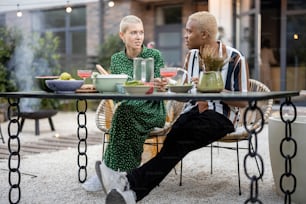 Multirassisches Paar redet und hat Spaß während eines Abendessens in ihrem Garten des Landhauses. Idee eines herzlichen Gesprächs und einer Beziehung. Lateinamerikanischer Mann und Europäerin genießen Zeit miteinander