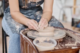 Nahaufnahme einer jungen kreativen Handwerkerin, die in der Töpferei geschult ist und neue Tongegenstände herstellt, während sie in der Werkstatt am rotierenden Rad sitzt