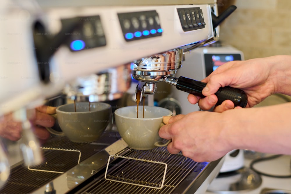 Close-up of professional barista holding cup and preparing coffee in a carob coffee machine in cafe