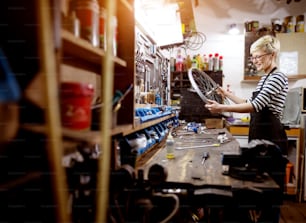 Hardworking professional smiling woman checking bare bicycle wheel in the workshop.