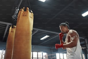 Gimnasio. Hombre cerca del saco de boxeo. Deportista asiático que va a golpear el equipo de boxeo en el gimnasio. Retrato De Chico Guapo Sexy Con Cuerpo Fuerte, Saludable Y Musculoso.