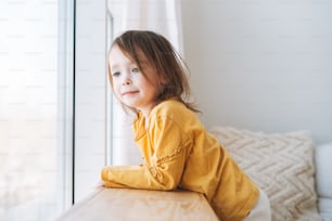 Cute little toddler girl in yellow longsleeve looking in window at the home
