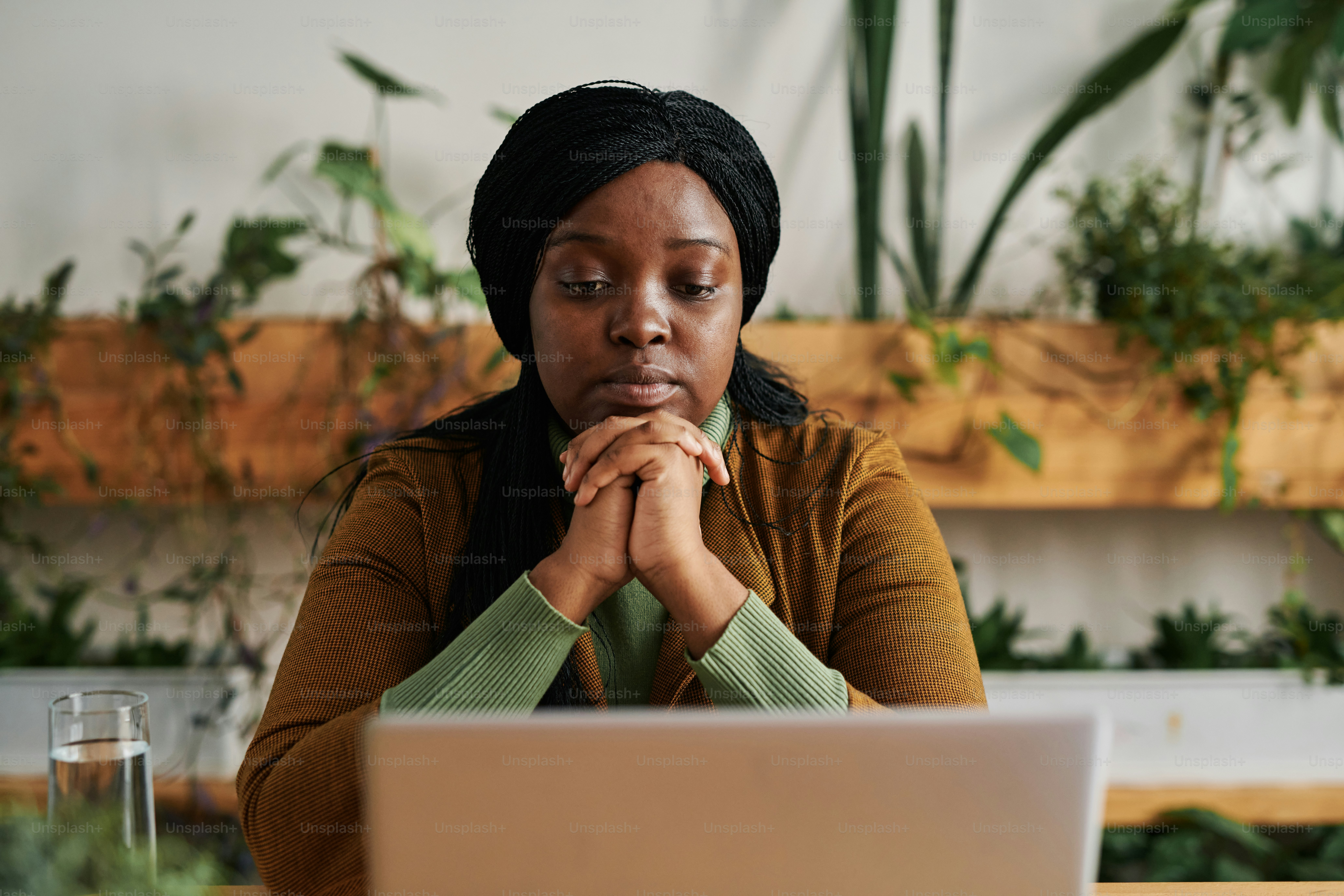Young serious female psychotherapist sitting in front of laptop screen in office and listening to patient during online psychological session