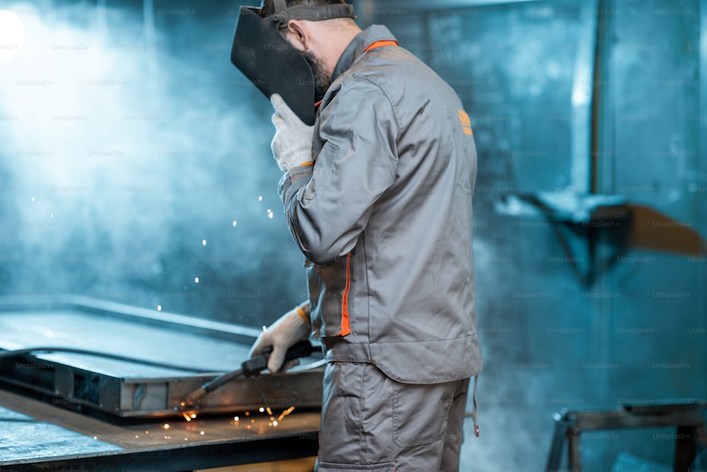 Welder in apron and protective mask having some welding job at the workshop. High quality photo