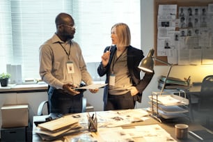 Young serious African American male FBI agent listening to mature female colleague in formalwear with pen by her chin