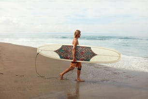 Surfeur. Bel homme de surf avec planche de surf blanche marchant sur une plage de sable. Sport nautique pour un mode de vie actif sur un beau fond d’océan.