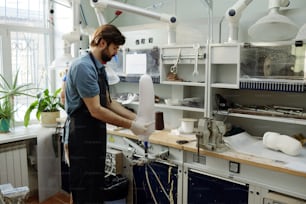 Arbeiter der Manufaktur legt weißes Blech auf das Werkstück der Prothesenpfanne, um seine Form nach Arbeitsplatz zu formen und zu fixieren
