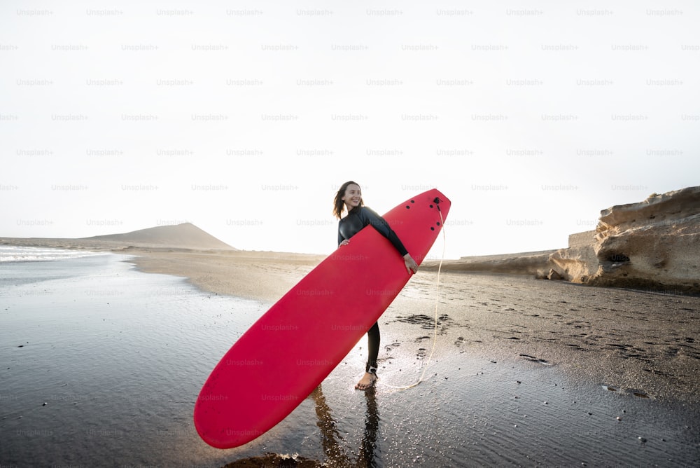 Giovane surfista in muta che corre con tavola da surf al mare. Attività estive e stile di vita attivo