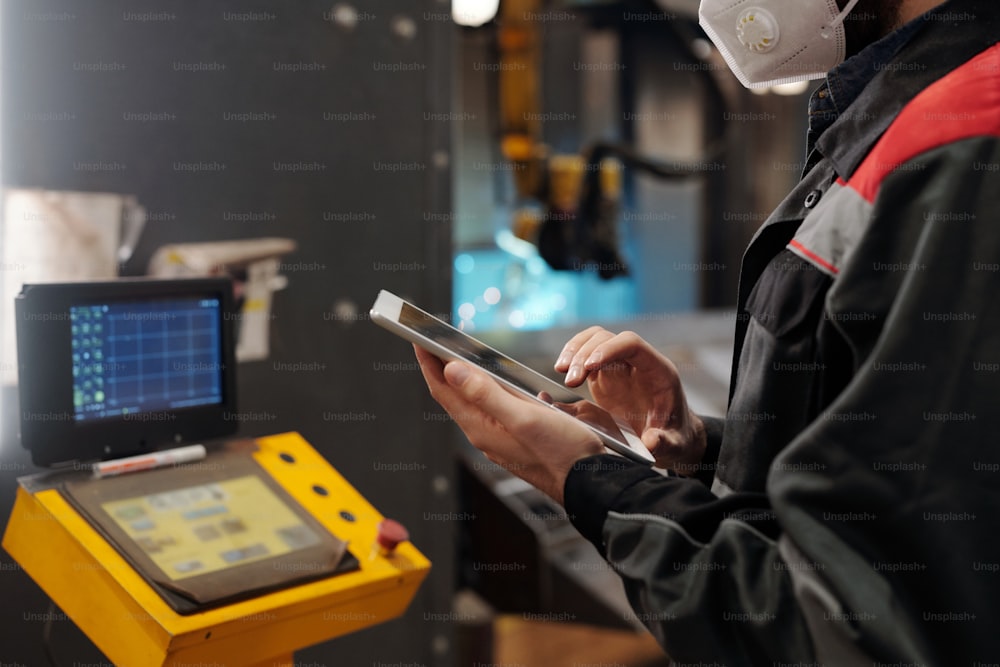 Young contemporary engineer in protective workwear holding digital tablet while scrolling through online technical data