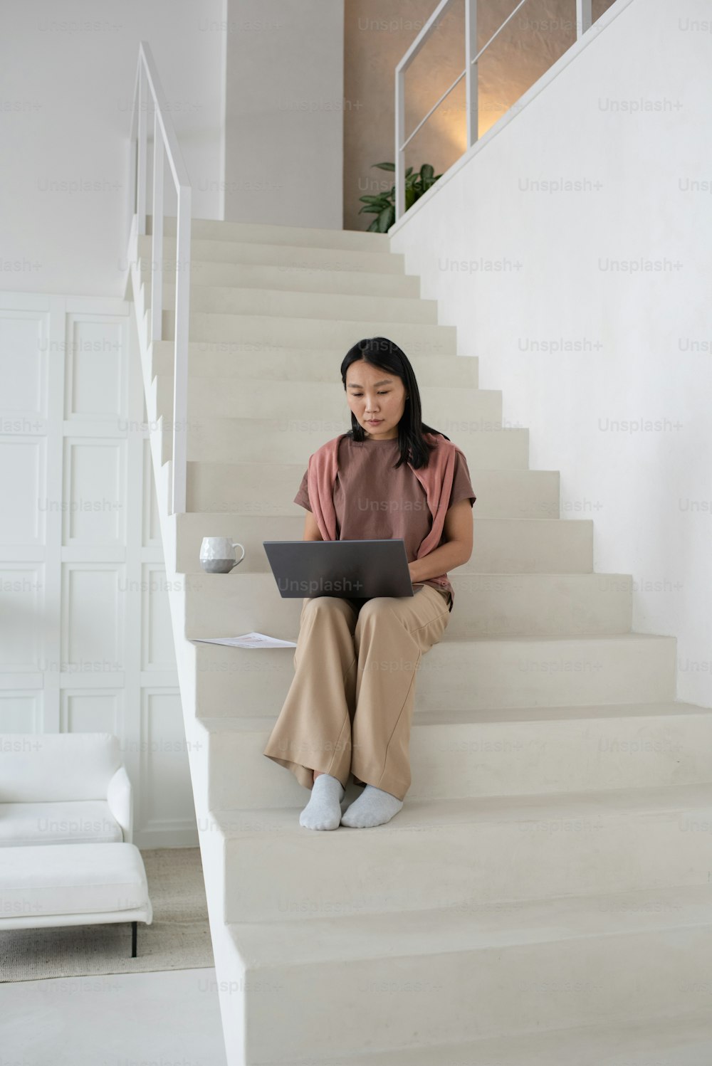 Young serious businesswoman with laptop concentrating on making presentation of new project while sitting on white staircase