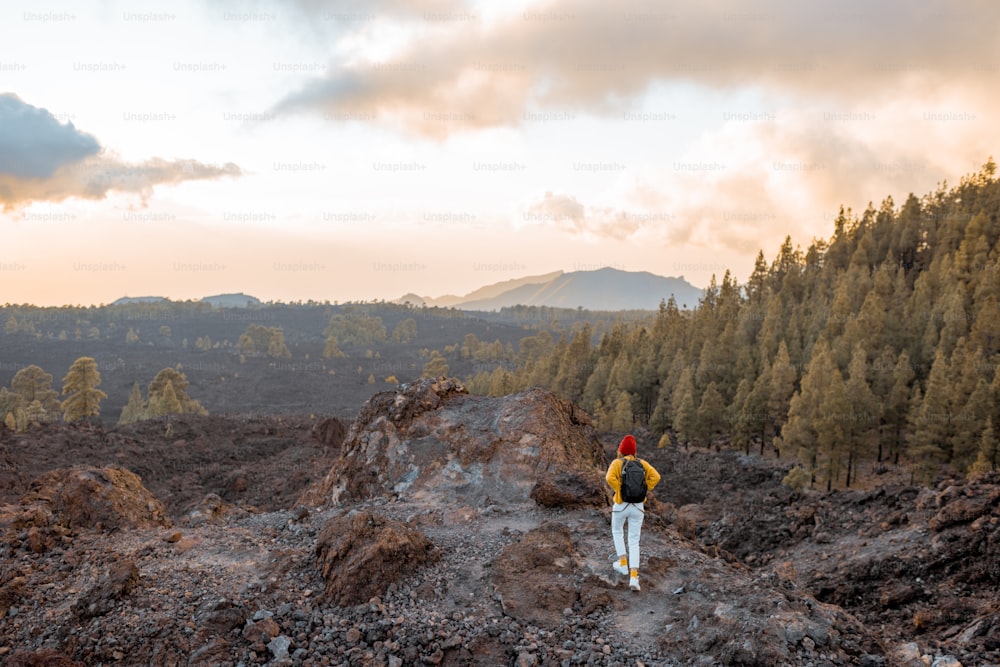 Paisajes volcánicos en una puesta de sol, mujer caminando en la tierra rocosa mientras viaja en la isla