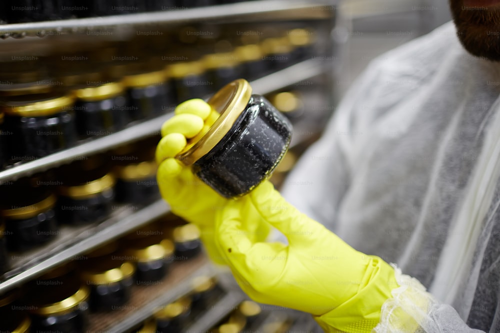 Seafood factory expert in gloved holding small jar with black caviar
