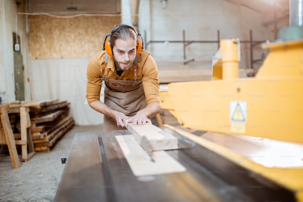 Carpentry worker sawing wooden planks with circular saw in the joinery warehouse