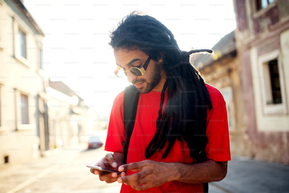 Young tourist man with dreadlocks and sunglasses holding mobile in his hand.