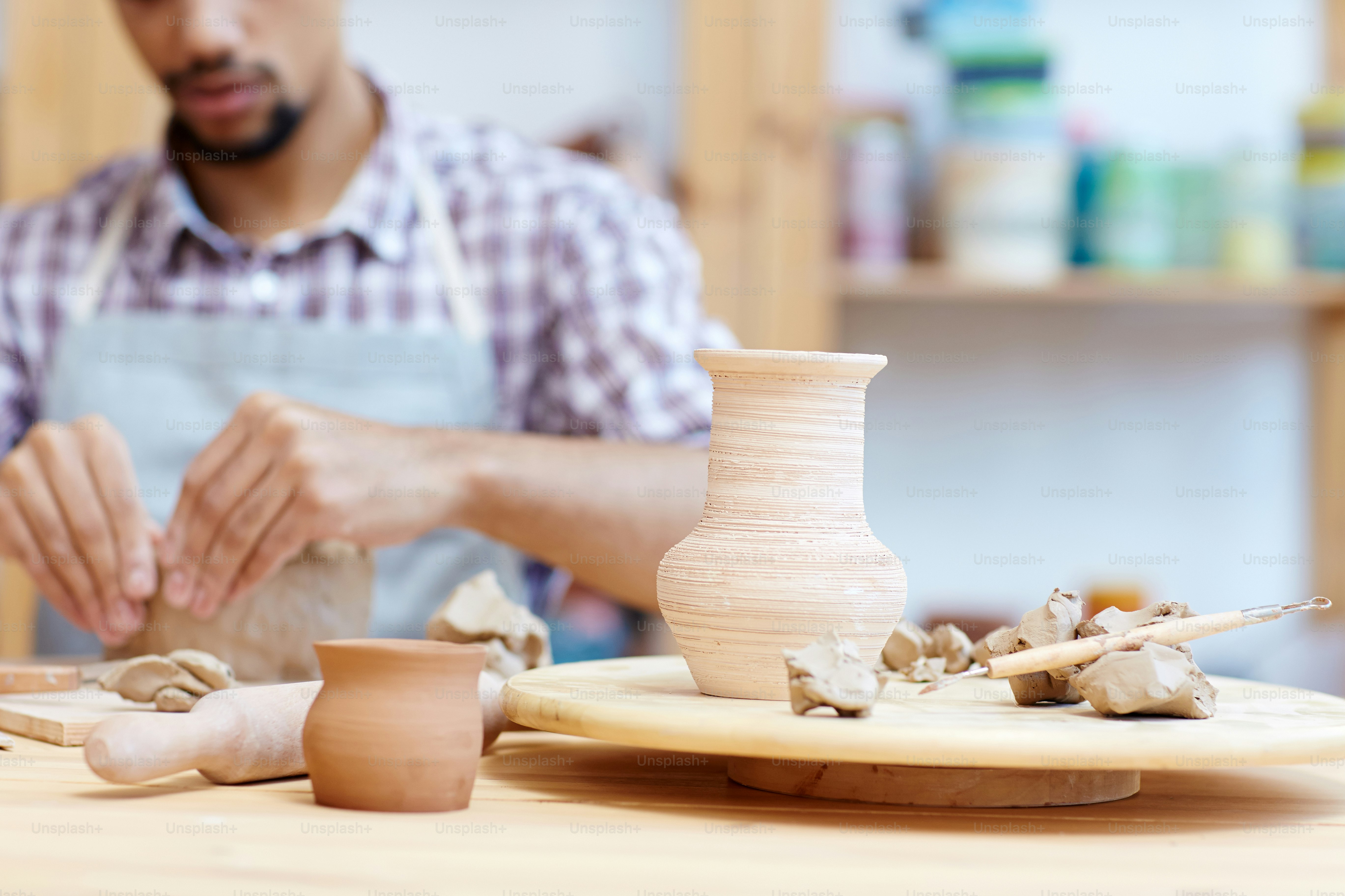 Defokussierter männlicher Keramiker Modelliertopf in der Werkstatt, schöne handgefertigte Tonvase im Vordergrund