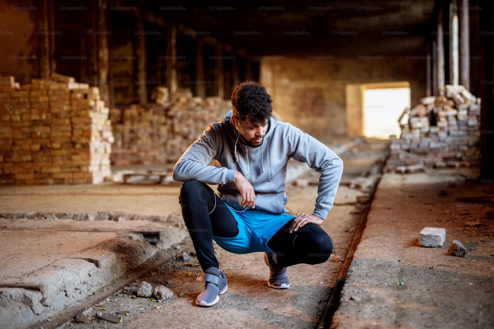 Portrait of focused motivated afro-american young handsome sportive man with earphones standing inside of the abandoned place. Successful young active man portrait.