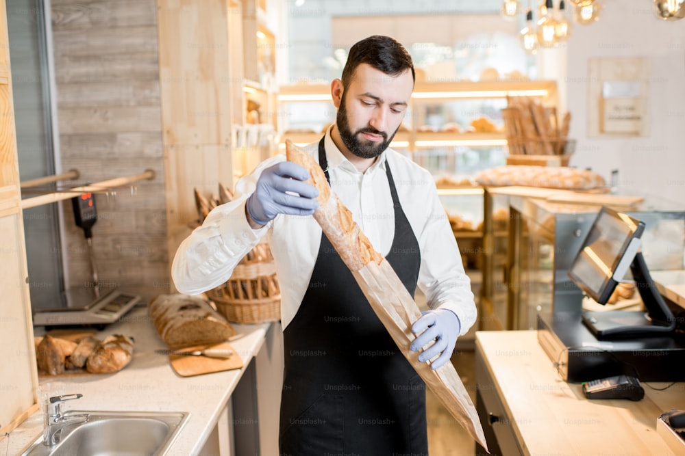 Portrait of a bread seller standing with baguette in the beautiful store with bakery products