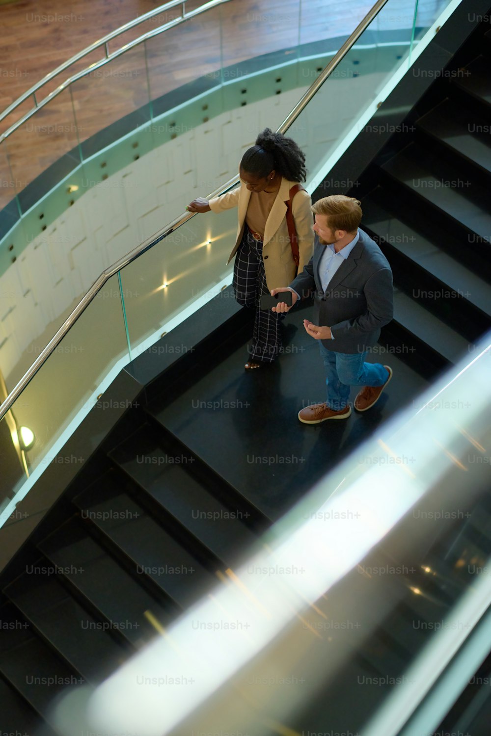 Above view of two young intercultural colleagues in formalwear moving downstairs along staircase and discussing working points