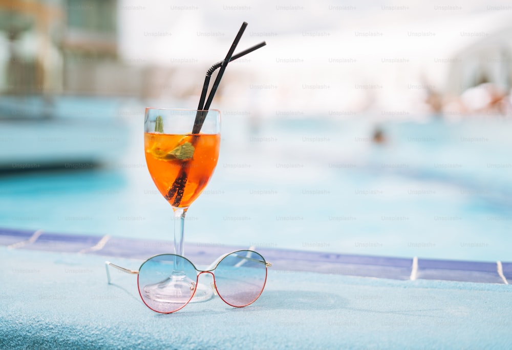 Glass of cocktail with ice and sunglasses on hotel pool, summer vacation
