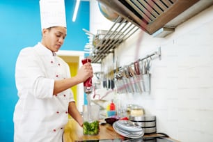 Young woman in chef uniform making broccoli smoothie with electric blender