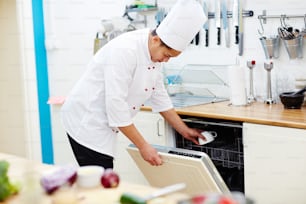 Chef de restaurante poniendo taza en lavadora de platos mientras trabaja en la cocina