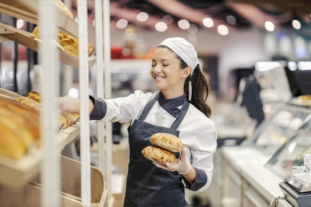Una vendedora arregla el pan y los pasteles en los estantes del supermercado.