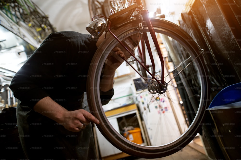Man closely examining bicycle wheel balance in the sunny workshop.