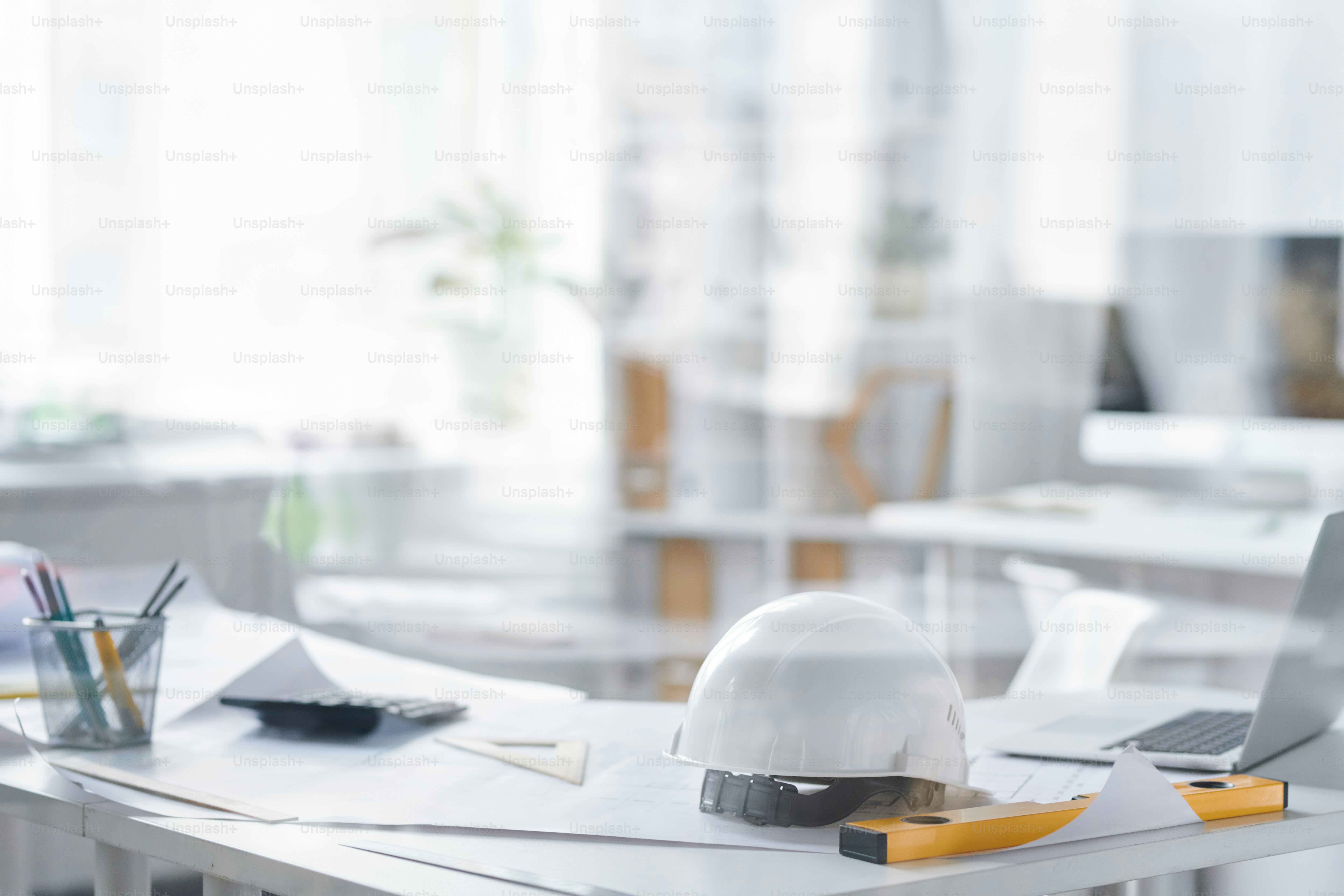 White hardhat, level check handtool, blueprints, laptop and pencils on desk of contemporary engineer or foreman in office