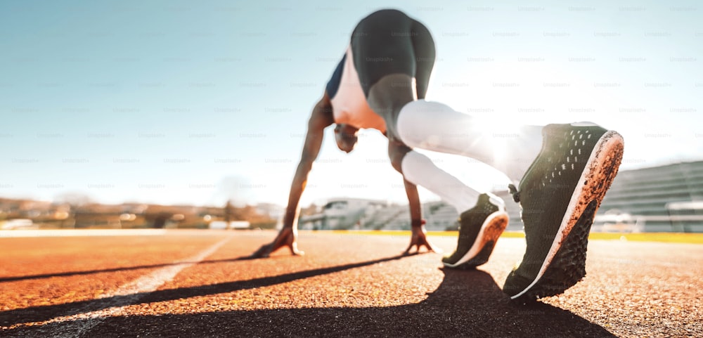 Afrikanischer Läufer läuft auf Laufband im Stadion - Füße auf Startblock bereit für einen Frühlingsstart - Nahaufnahme am Schuh