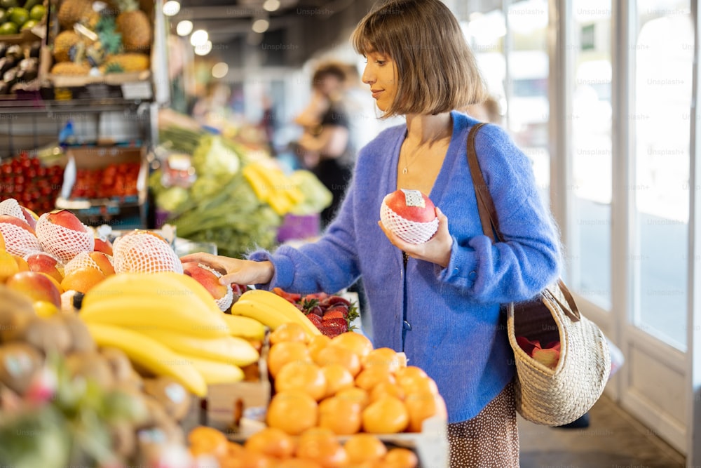 Mulher que toma manga do balcão do mercado local, enquanto compra frutas com saco de malha reutilizável. Sustentabilidade e conceito de alimentos orgânicos