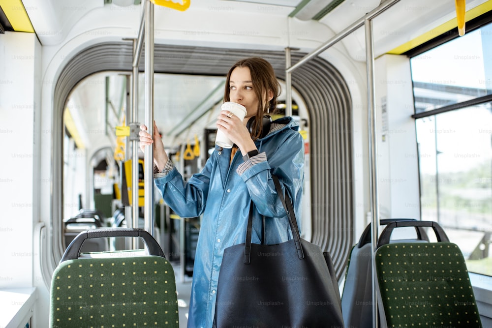 Mujer joven con estilo que disfruta del viaje en el tranvía moderno, de pie con café en el transporte público