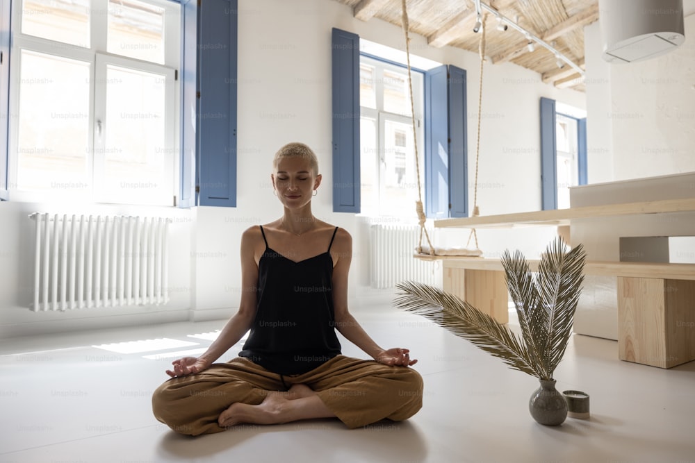 Jeune femme élégante méditant et pratiquant le yoga dans un salon moderne et lumineux à la maison. La pleine conscience, se sentir calme dans une maison moderne