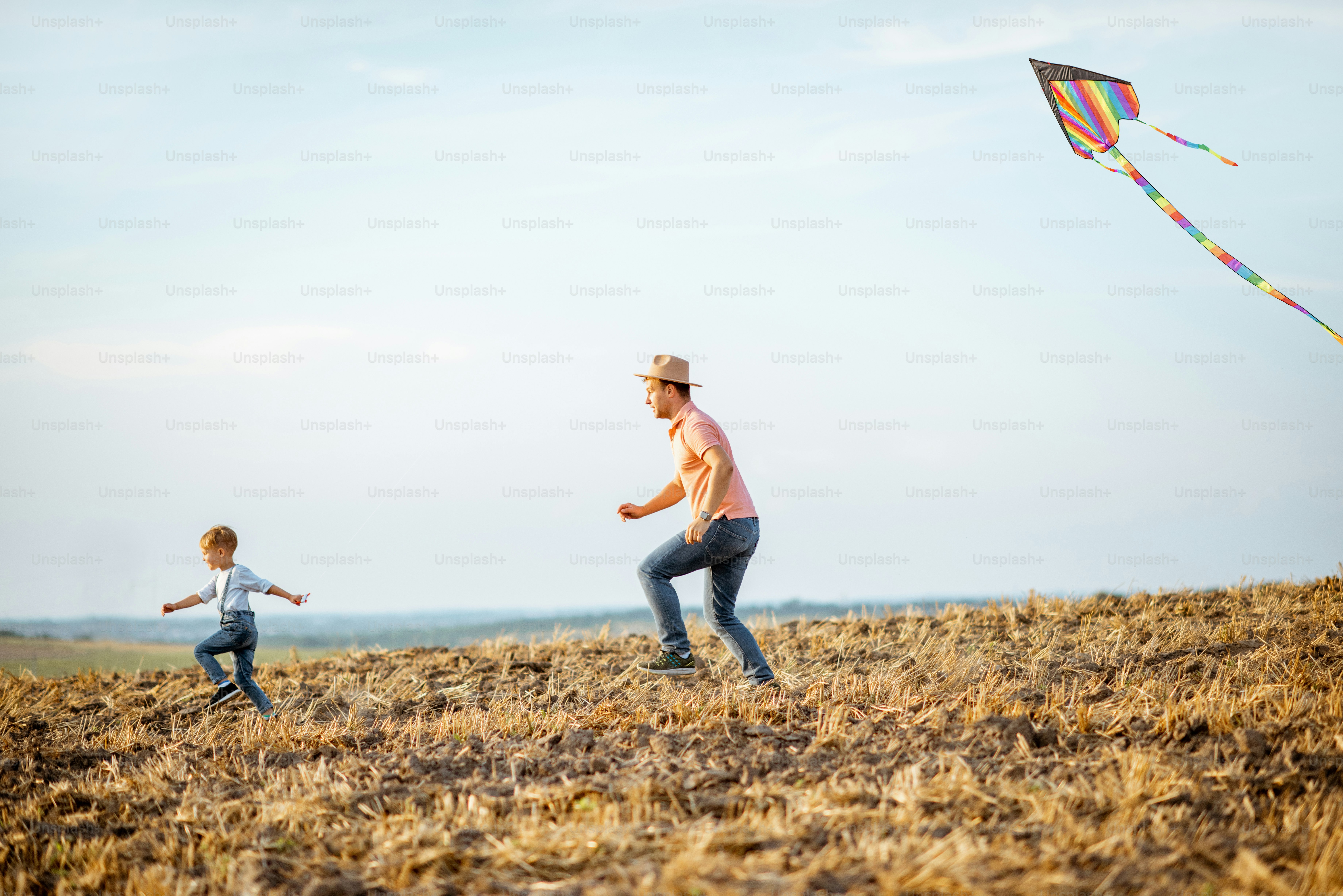 Father with son launching colorful air kite on the field. Concept of a happy family having fun during the summer activity