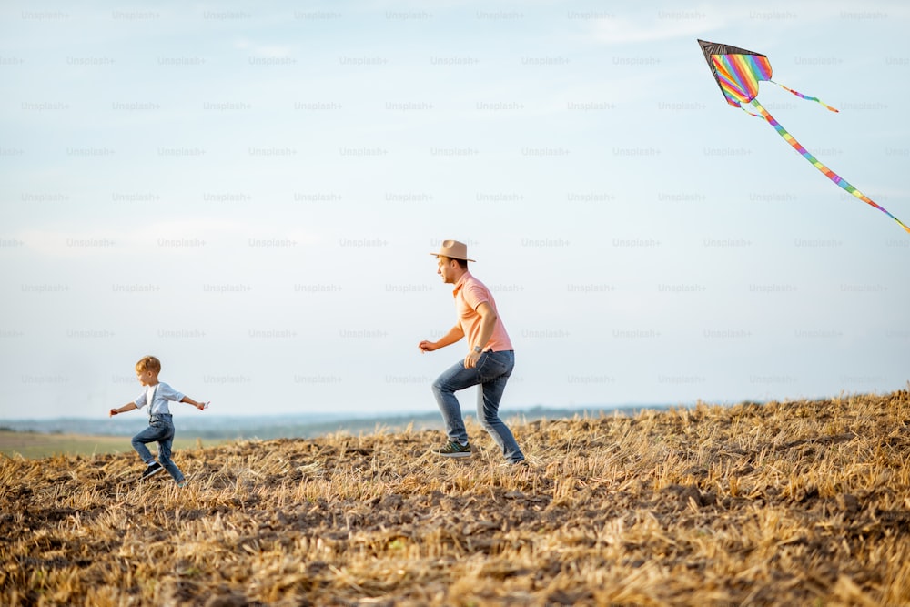 아들과 함께 아버지가 들판에서 화려한 공기 연을 발사합니다. 여름 활동 동안 즐거운 시간을 보내는 행복한 가족의 개념