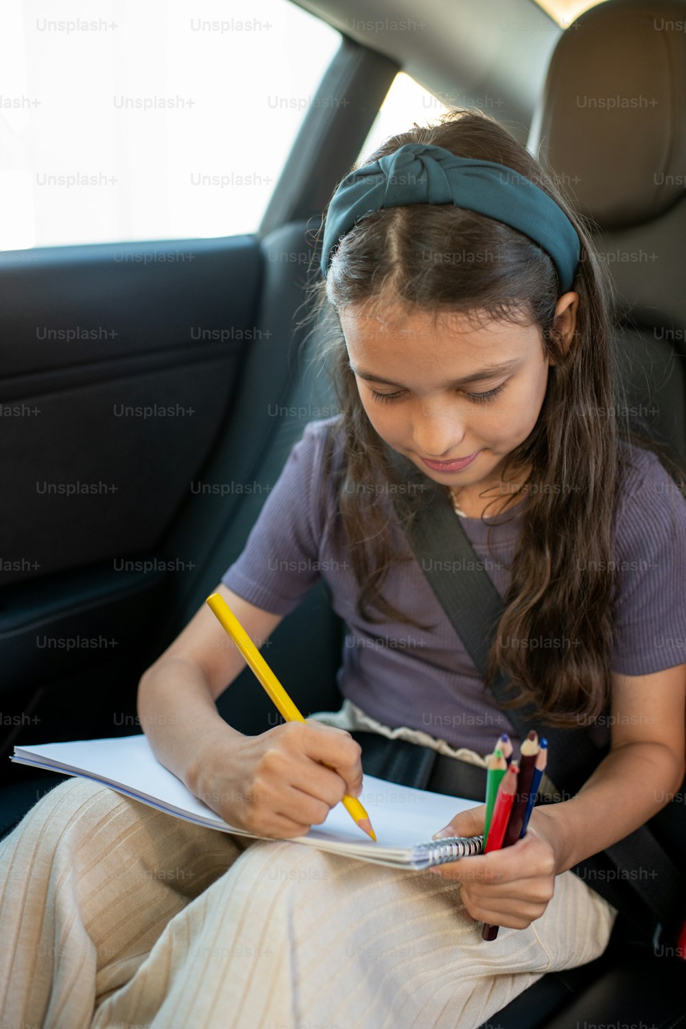 Cute schoolgirl drawing with colorful crayons on backseat of electric car