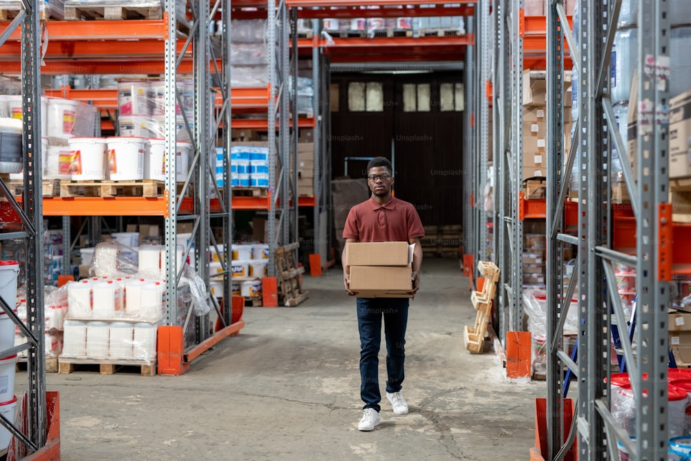 Joven trabajador africano de almacén que transporta cajas