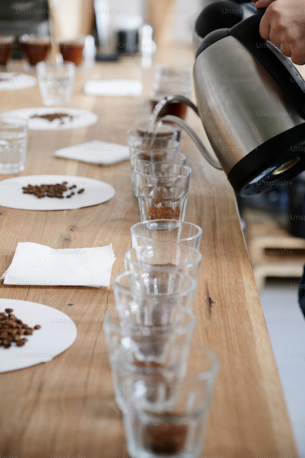 Nahaufnahme von Barista, der kochendes Wasser in Glastassen mit gemahlenem Kaffee aus zwei Wasserkochern schmollt und frischen Kaffee für die Verkostung untersucht. Porträt im selektiven Fokus