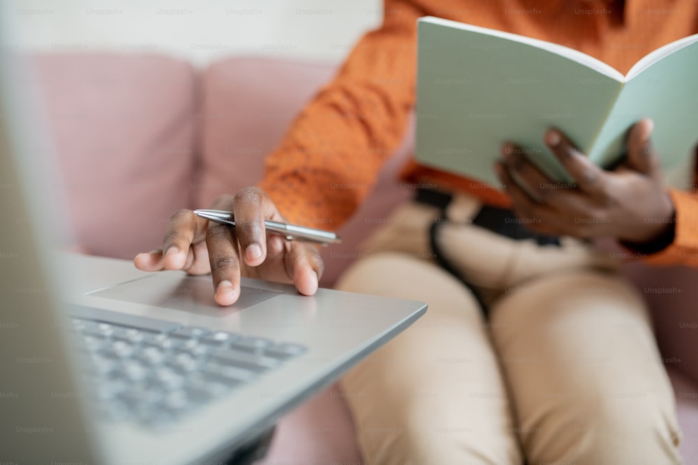 ノートパソコンの前に座って学習しながら、キーパッドでパネルに触れるペンを持つ若いアフリカの女性の手