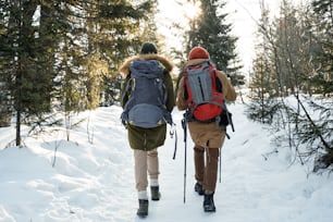 Back view shot of two unrecognizable young people wearing backpacks hiking in mountains on winter day