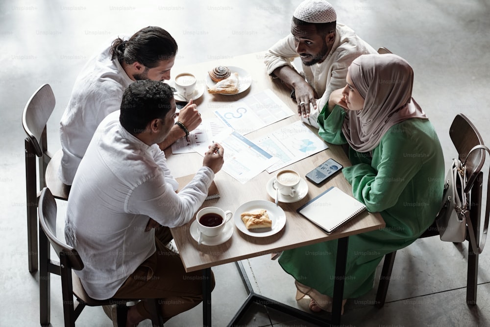 Grupo de jovens colegas muçulmanos sentados à mesa e debatendo sobre estratégia durante o almoço