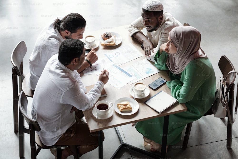 Group of young Muslim colleagues sitting at table and brainstorming about strategy during lunch