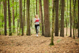 Junge Sportlerin rennt beim Training am Sommermorgen den Waldweg zwischen Bäumen hinunter