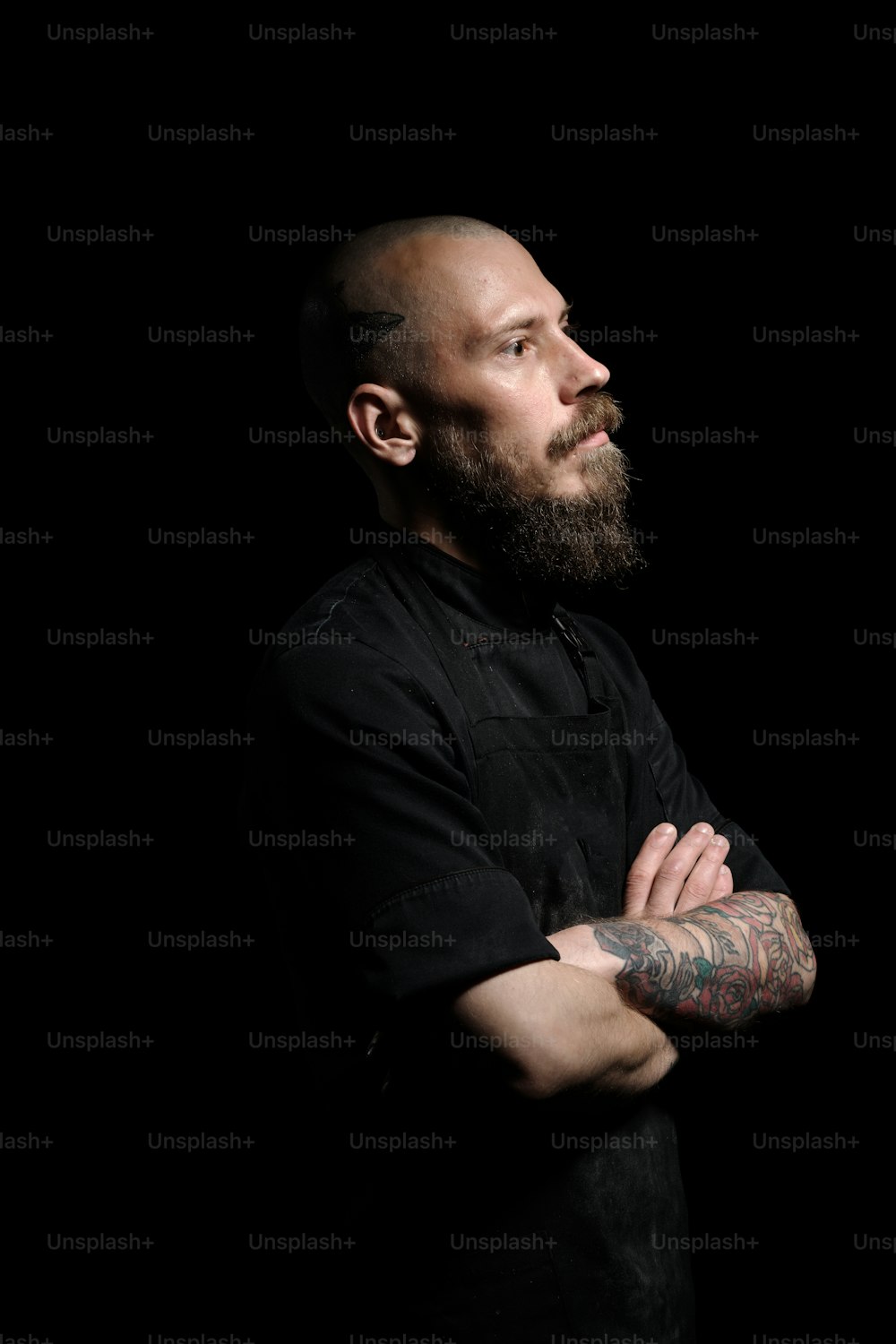 Portrait of brutal bold bearded chef in studio. He is looking straight to camera, hands crossed on chest