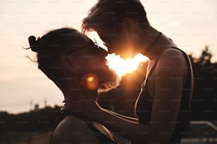 Close up portrait of young couple in round glasses with colorful hair kissing outdoor in sunset natural light. Sunbeam shines between them